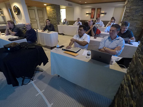Meeting room with distributors seated at tables with laptops, facing a projector