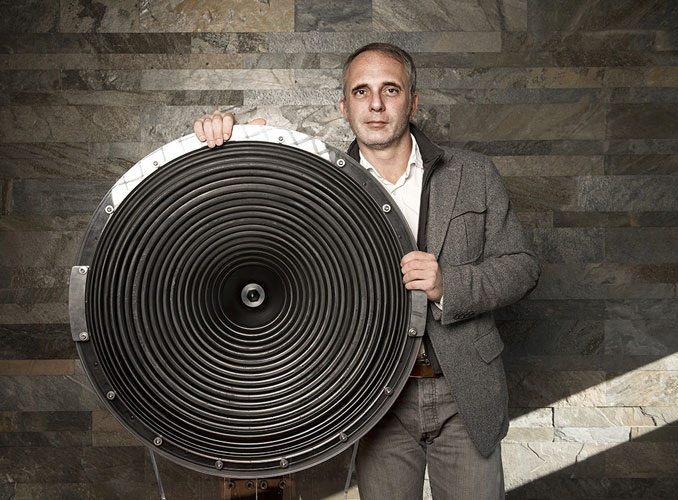 Claudio Lastrucci holding a large loudspeaker cone against a stone wall