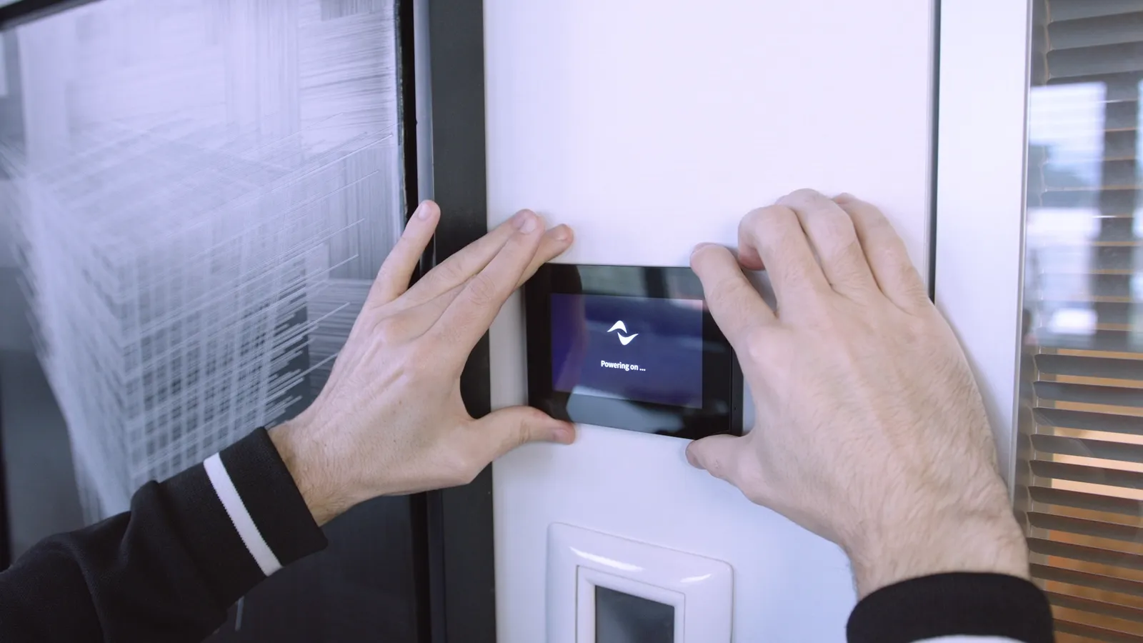 Hands fitting a WM Touch panel to a wall; the screen shows Powering on