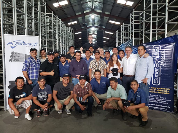 Seminar attendees posing in a warehouse with truss, between Powersoft and SuperSonidos banners