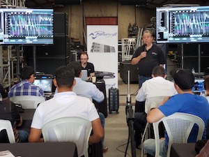 Seminar: a speaker with a microphone addresses seated attendees; two screens show software