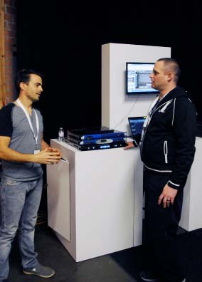 Two men talking beside a display stand with Powersoft amplifiers and a monitor