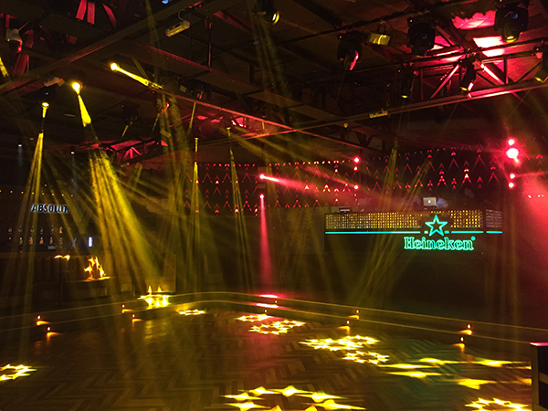 Banana nightclub dance floor lit by moving-head beams, with a bar under a Heineken sign