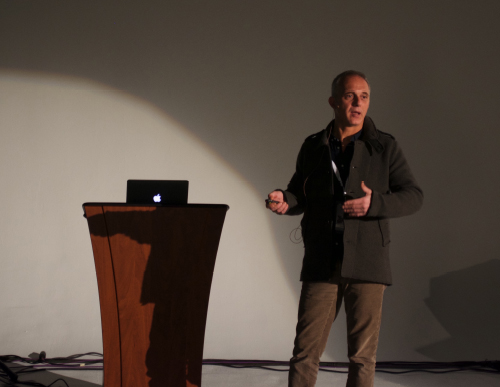 Claudio Lastrucci presenting beside a wooden lectern with a laptop