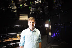 Man standing in a dark room with loudspeakers mounted on the walls and ceiling