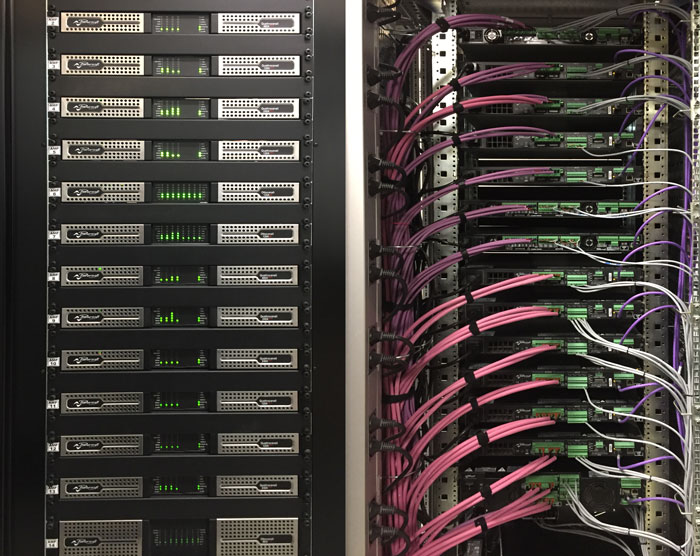 Powersoft install amplifiers in a rack, next to a rack rear wired with pink and purple cables