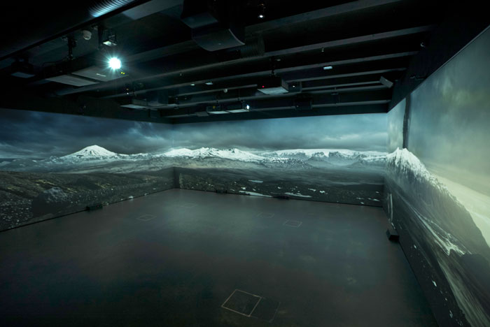 Dark room with a panoramic projection of snow-capped mountains across three walls