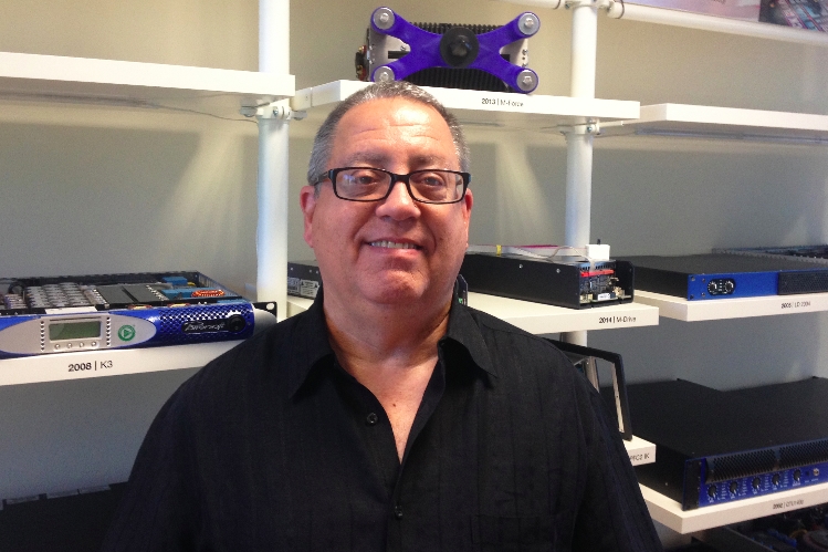 Gilberto Morejon in front of shelves of Powersoft products labelled by year, including K3, M-Drive and M-Force